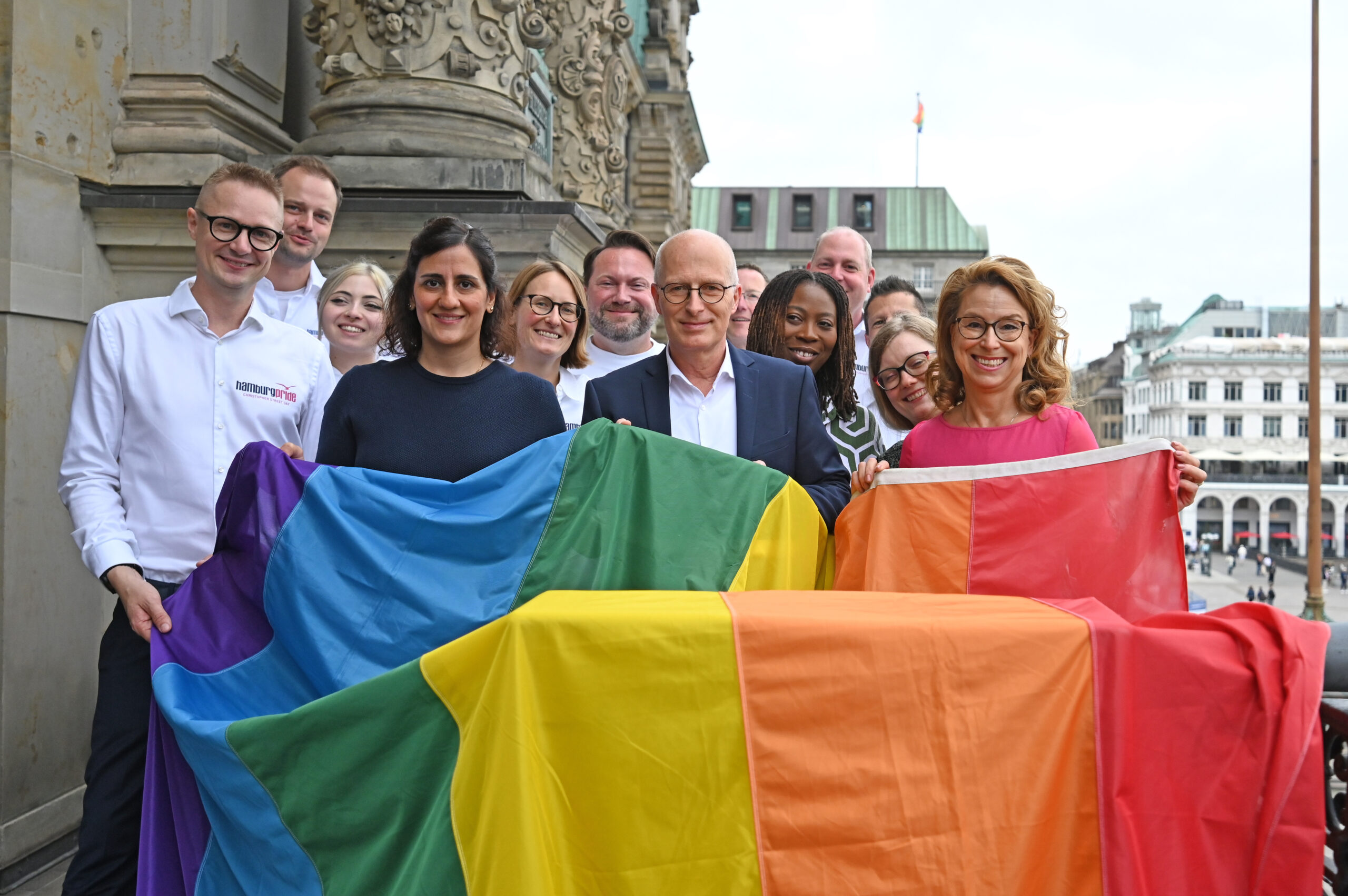 Maryam Blumenthal (Bündnis 90/Die Grünen, vorne, 2.v.l.), Wissenschaftssenatorin von Hamburg, Peter Tschentscher (SPD, vorne, 3.v.l.), Hamburgs Erster Bürgermeister und Carola Veit (SPD, vorne, r), Präsidentin der Hamburgischen Bürgerschaft, halten eine Regenbogenflagge auf dem Balkon des Hamburger Rathauses. Zum Auftakt der Pride Week 2025 weht die Regenbogenflagge am Hamburger Rathaus.