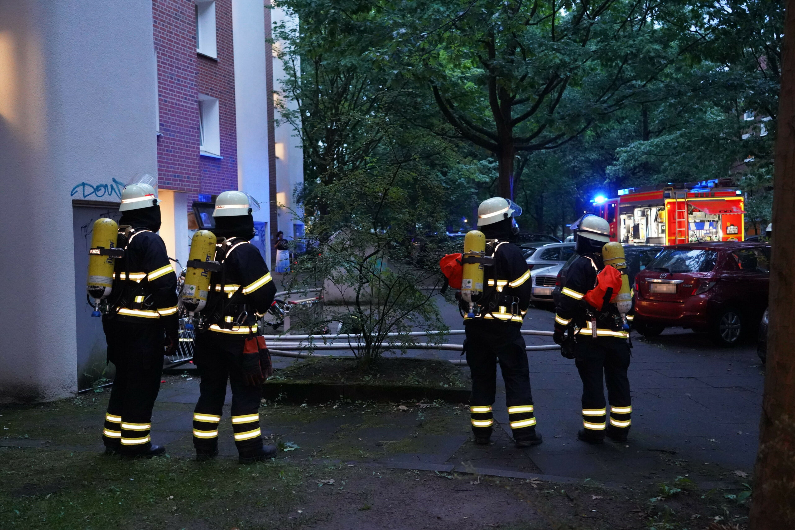 Einsatzkräfte der Feuerwehr stehen vor dem Mehrfamilienhaus.