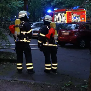 Einsatzkräfte der Feuerwehr stehen vor dem Mehrfamilienhaus.