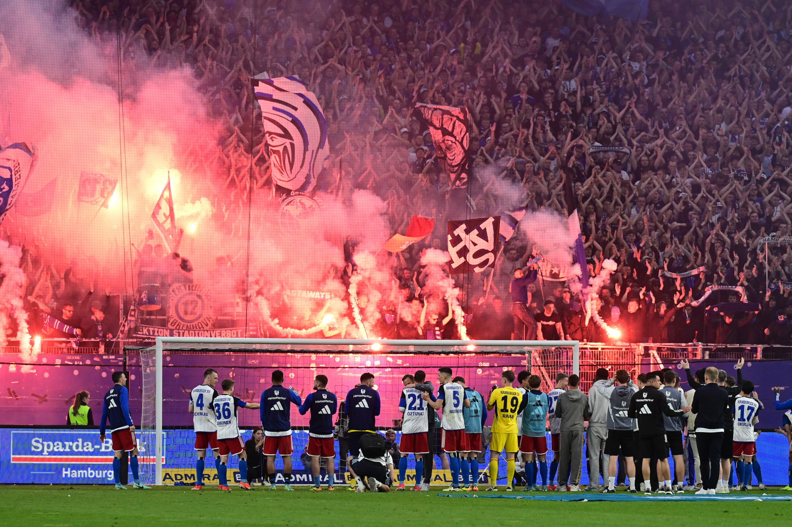HSV-Profis vor der Nordtribüne, auf der Pyrotechnik gezündet wird