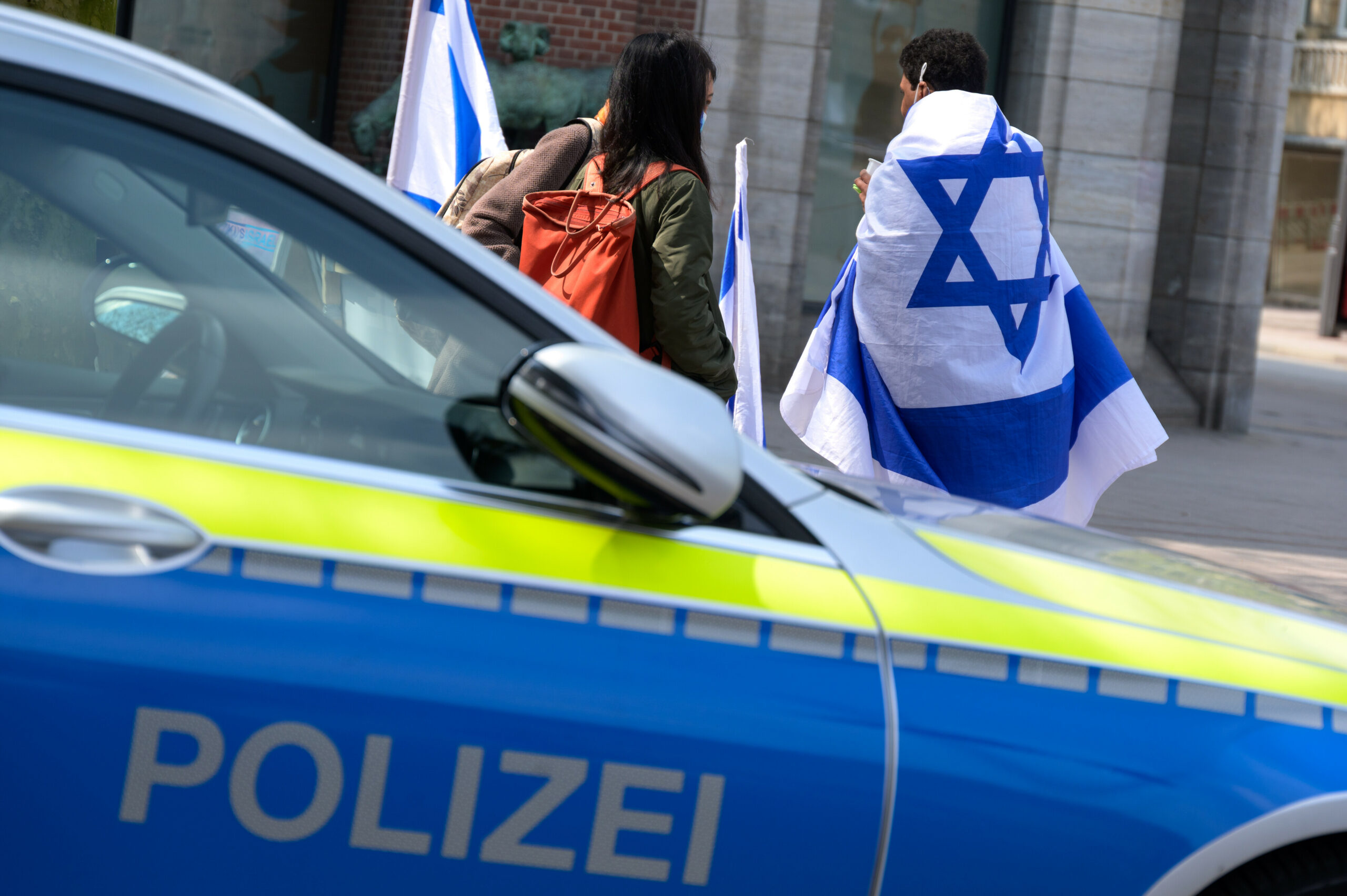 Mehrere Menschen stehen mit Israel-Flaggen als Teil einer Mahnwache in der Innenstadt neben einem Streifenwagen. Aufnahmedatum