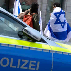 Mehrere Menschen stehen mit Israel-Flaggen als Teil einer Mahnwache in der Innenstadt neben einem Streifenwagen. Aufnahmedatum