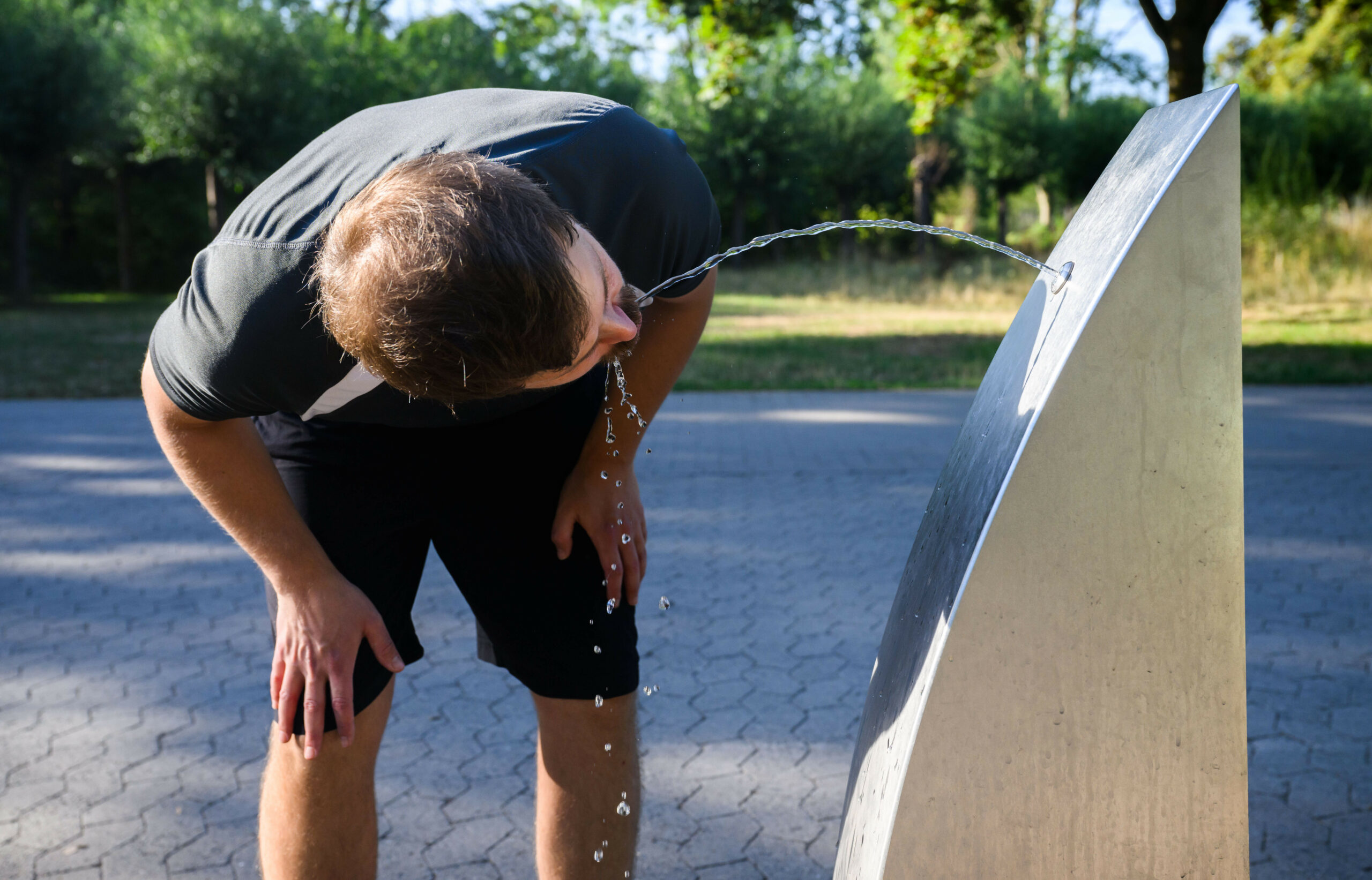 Ein Mann trinkt aus einem Trinkbrunnen.