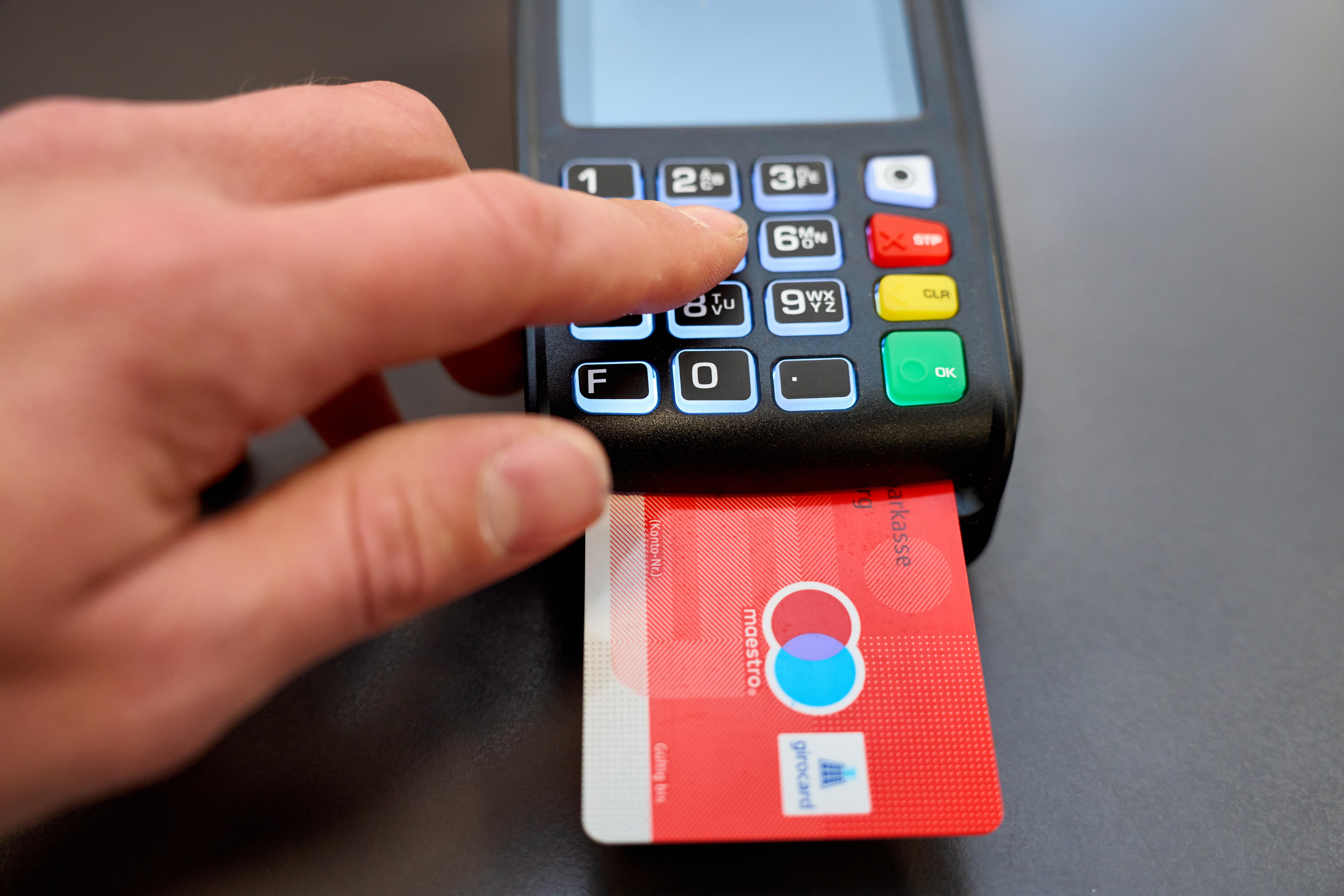 Mann gibt beim Bezahlen an der Kasse im Geschäft die PIN Geheimnummer in ein EC-Gerät ein.