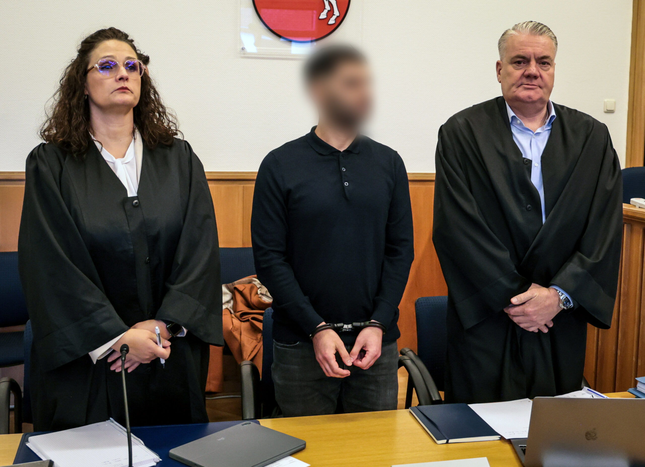 Der 35-jährige Angeklagte (M.) steht zwischen seinen Anwälten in einem Verhandlungssaal im Landgericht.
