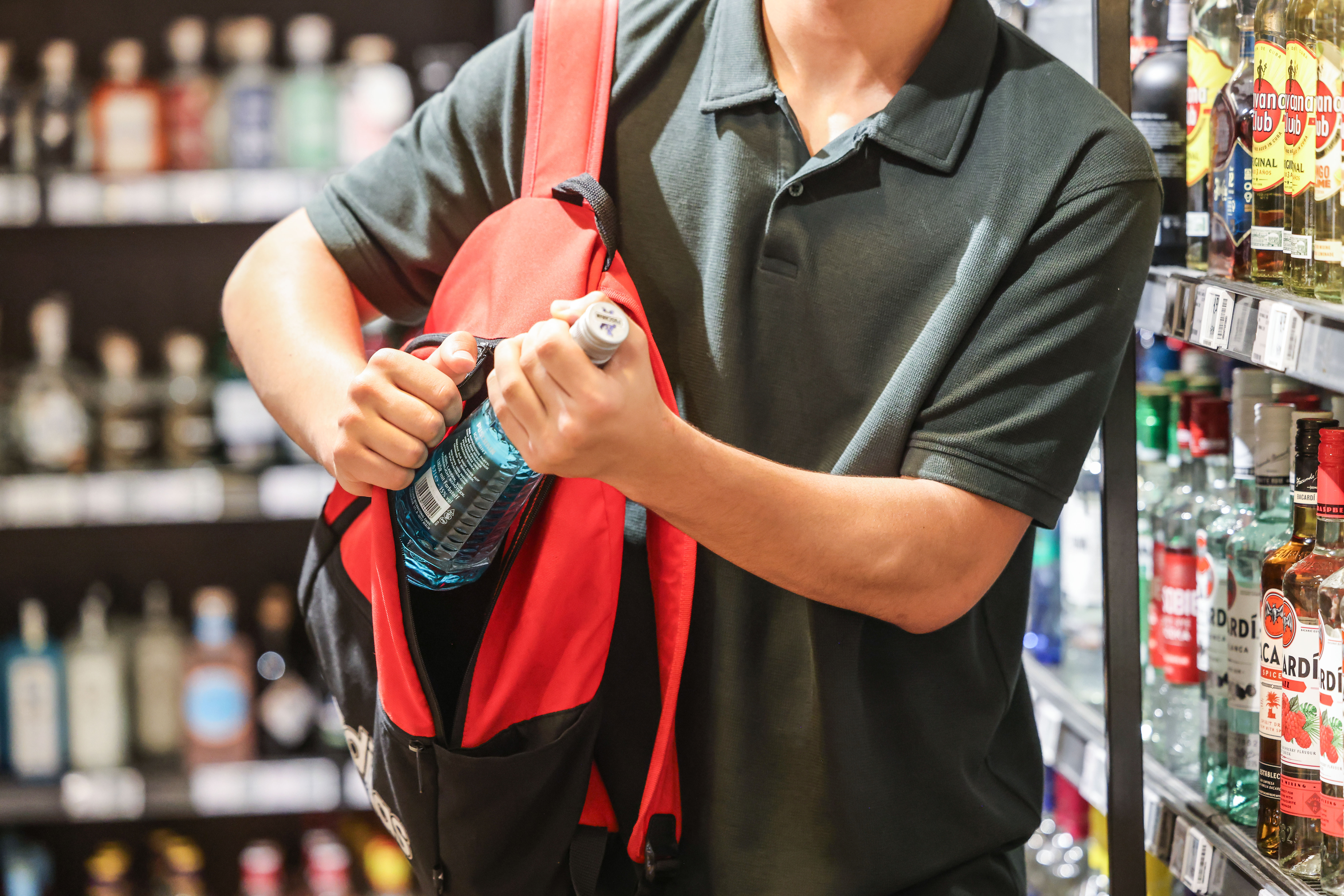 Ein Mann steckt in einem Supermarkt eine Flasche mit einem alkoholhaltigen Getränk in seinen Rucksack.