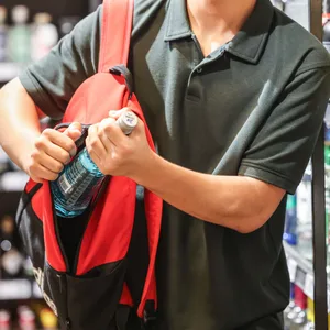 Ein Mann steckt in einem Supermarkt eine Flasche mit einem alkoholhaltigen Getränk in seinen Rucksack.
