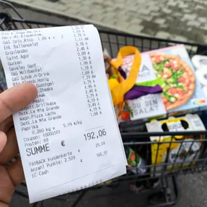 Ein voller Einkaufswagen mit Lebensmitteln und Haushaltswaren sowie ein Kassenbon.
