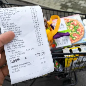Ein voller Einkaufswagen mit Lebensmitteln und Haushaltswaren sowie ein Kassenbon.