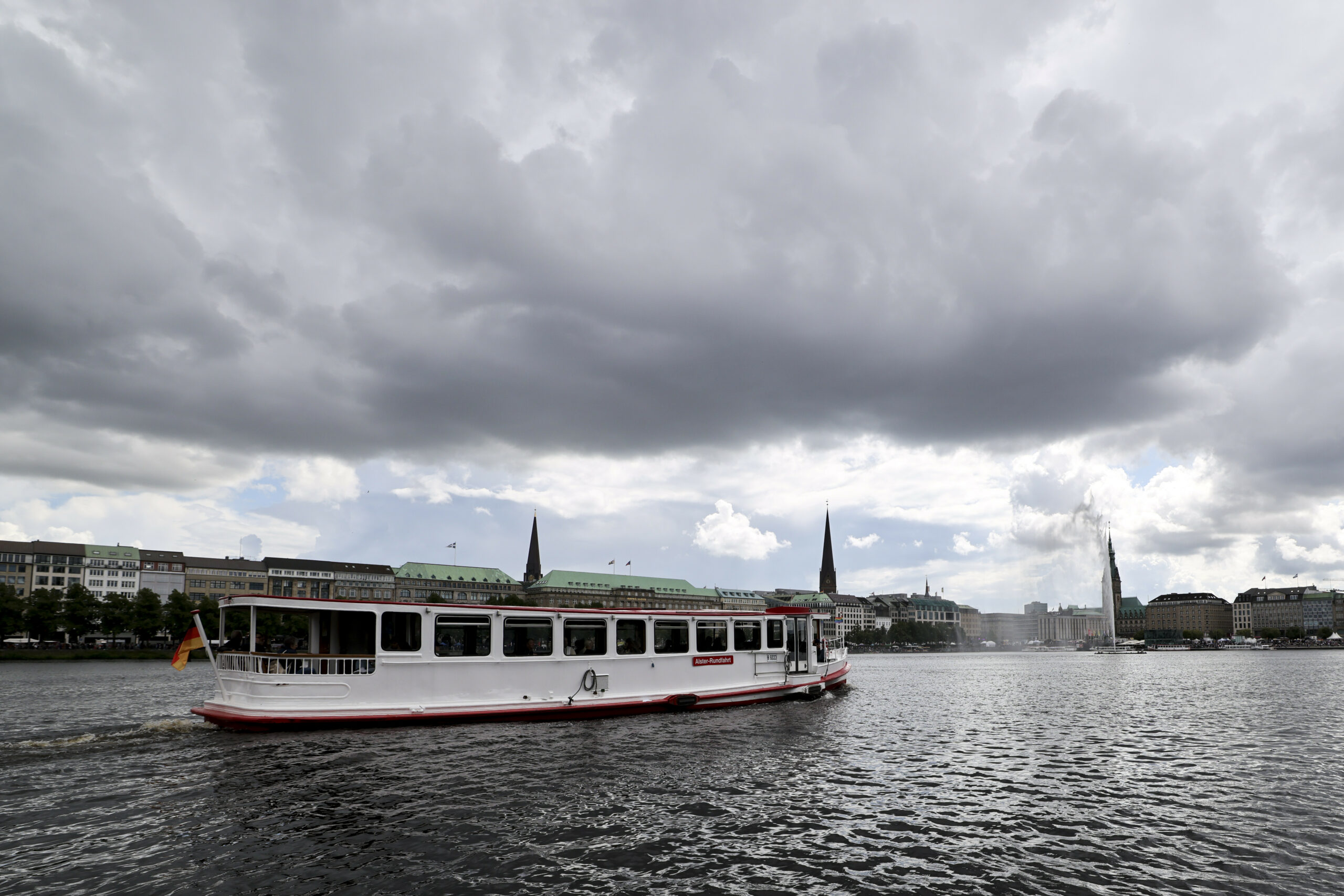 Ein Ausflugsschiff für Alster-Rundfahrten ist unter dunklen Wolken auf der Binnenalster unterwegs.