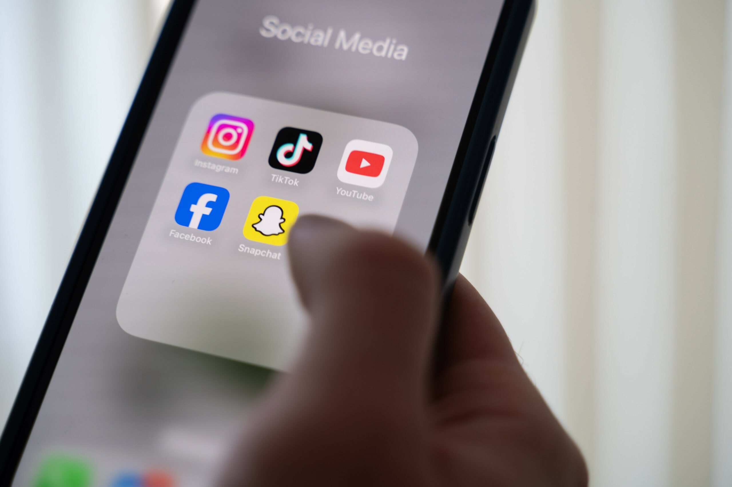Eine Frau hält ein Smartphone, auf dessen Display verschiedene Social Media Apps angezeigt werden