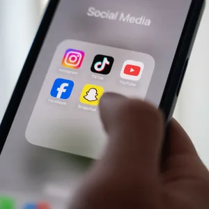Eine Frau hält ein Smartphone, auf dessen Display verschiedene Social Media Apps angezeigt werden