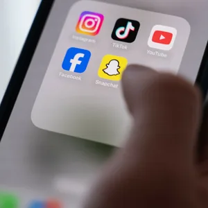 Eine Frau hält ein Smartphone, auf dessen Display verschiedene Social Media Apps angezeigt werden