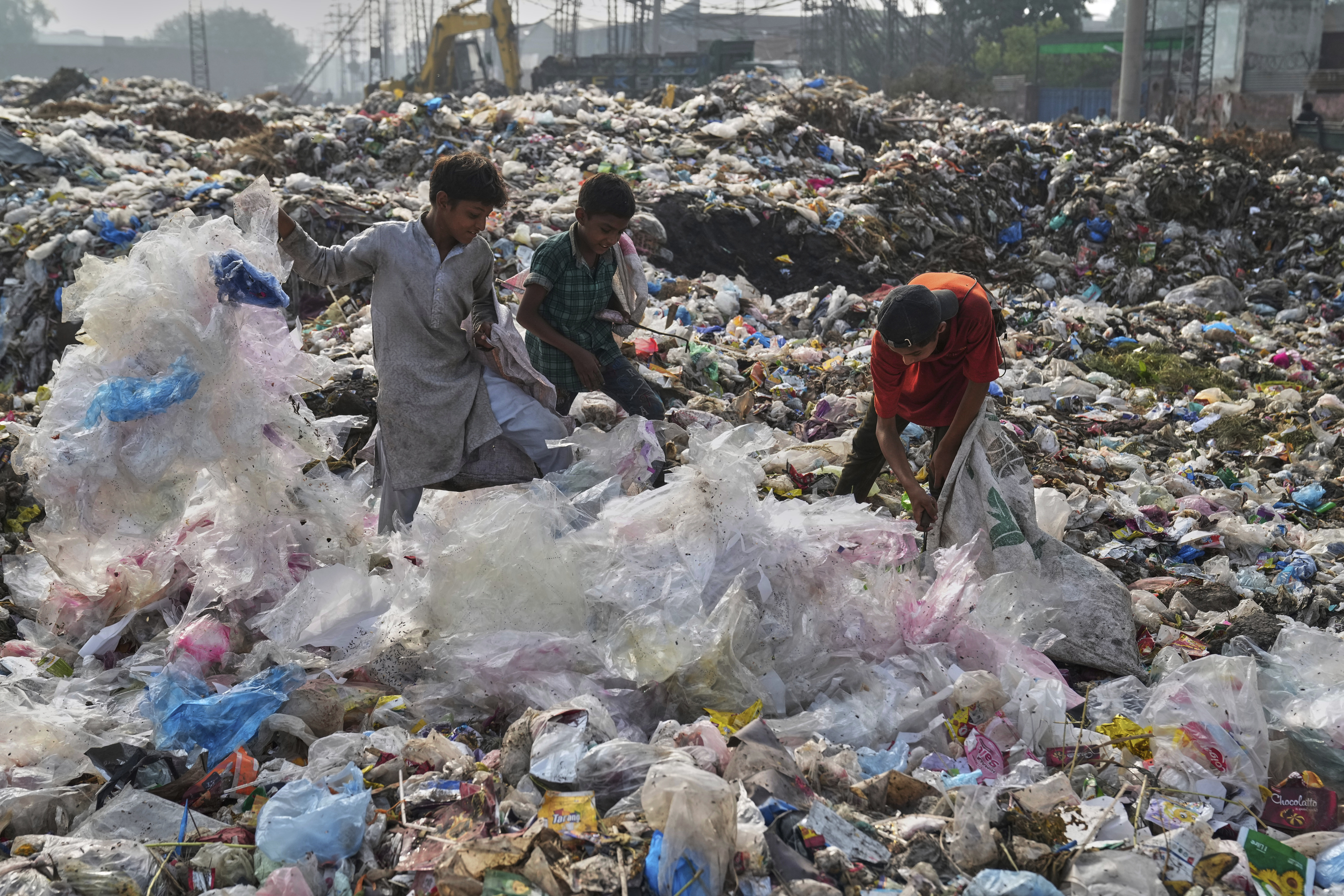 Drei Personen stehen auf einer riesigen Mülldeponie in Pakistan.