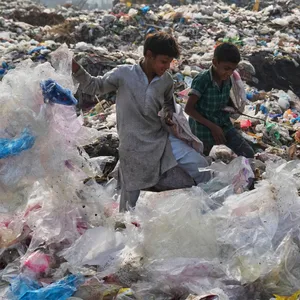 Drei Personen stehen auf einer riesigen Mülldeponie in Pakistan.