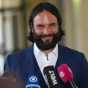 Mann mit dunklen Haaren vor Mikrofonen