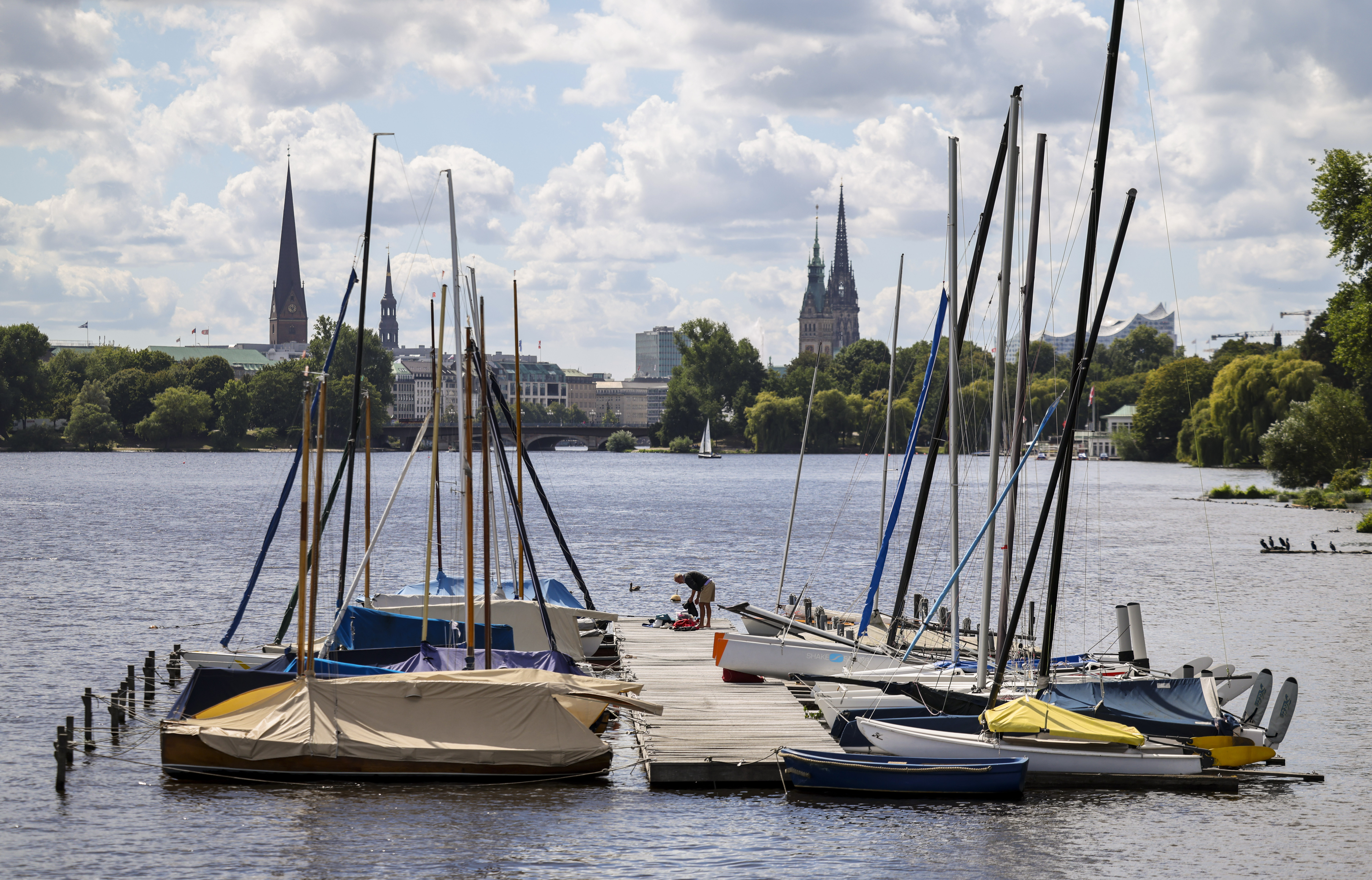 Ein Mann steht auf einem Steg auf der Alster am Anleger Rabenstraße und bereitet sein Segelboot für eine Fahrt vor.