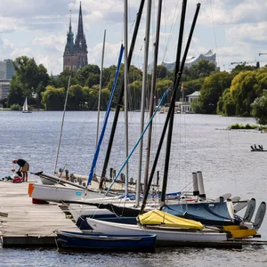 Ein Mann steht auf einem Steg auf der Alster am Anleger Rabenstraße und bereitet sein Segelboot für eine Fahrt vor.