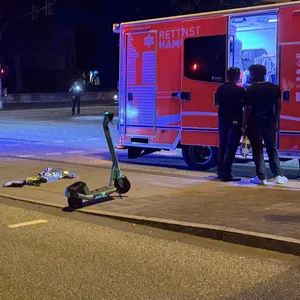 Ein schwarzer Audi steht an einer Ampel. Rechts von dem Auto steht der E-Scooter.