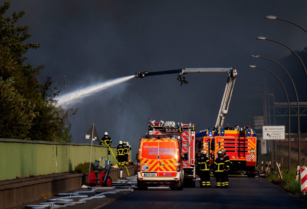 Feuerwehrleute stehen vor einer Rauchwand und versuchen, den Großbrand auf der Veddel zu bekämpfen