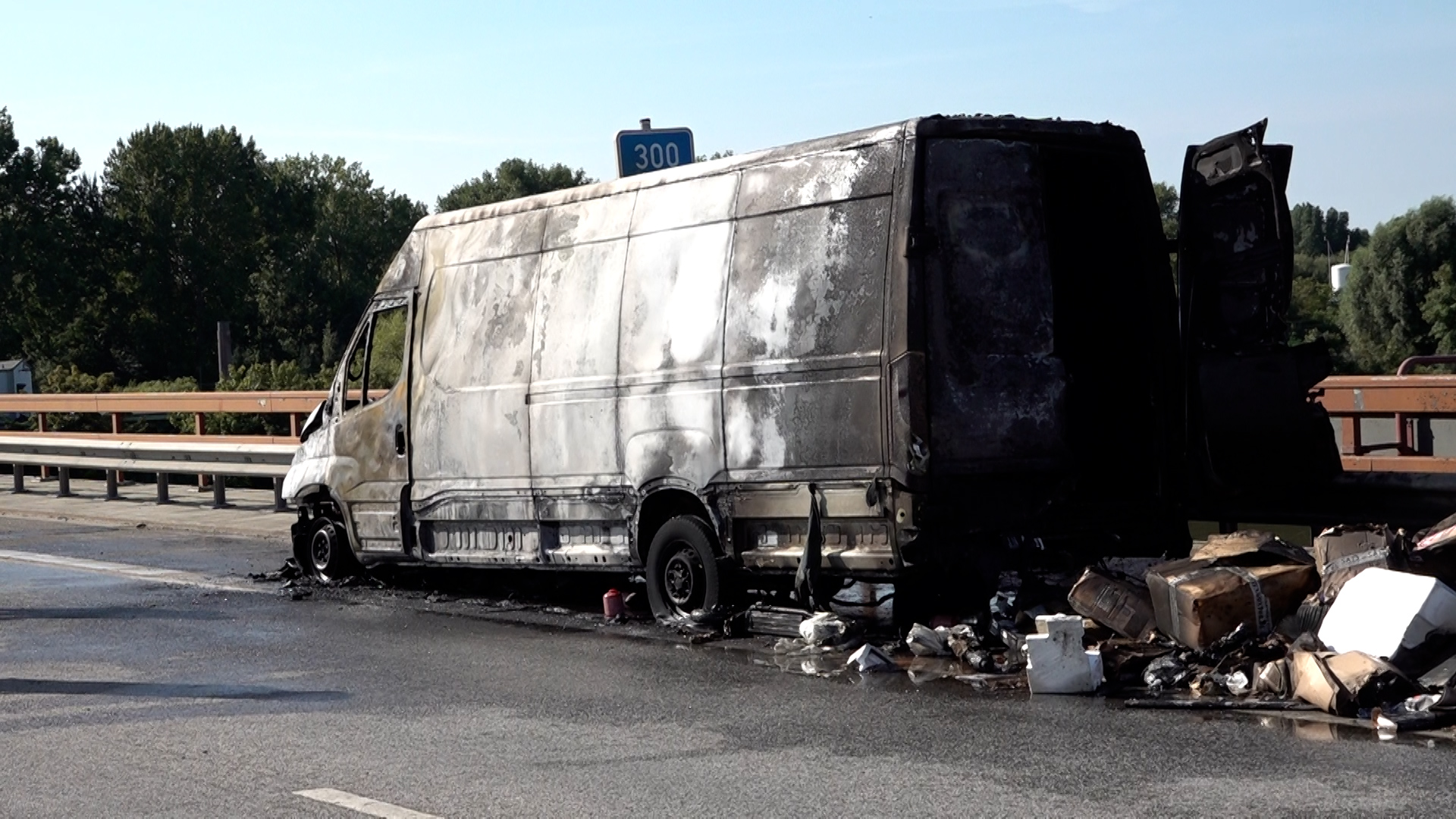 Verbrannte Pakete liegen auf der Straße neben dem ausgebrannten Transporter.