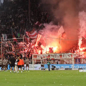 „Holt für uns den Derbysieg“ steht auf einem Banner im Fanblock, es brennt Pyrorechnik.