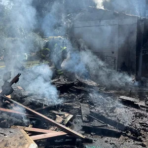 Feuerwehrkräfte stehen vor den rauchenden Überresten der abgebrannten Gartenlaube.