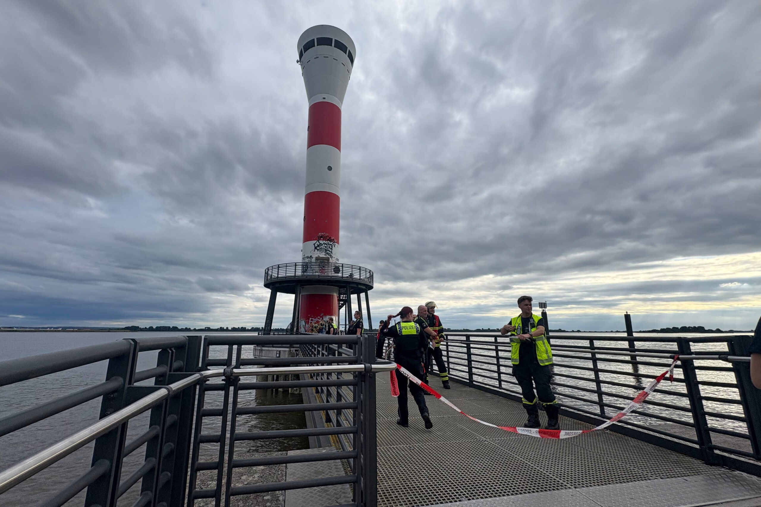 Polizisten und Einsatzkräfte der Feuwerwehr stehen an einem Leuchtfeuer an der Elbe in Hamburg.