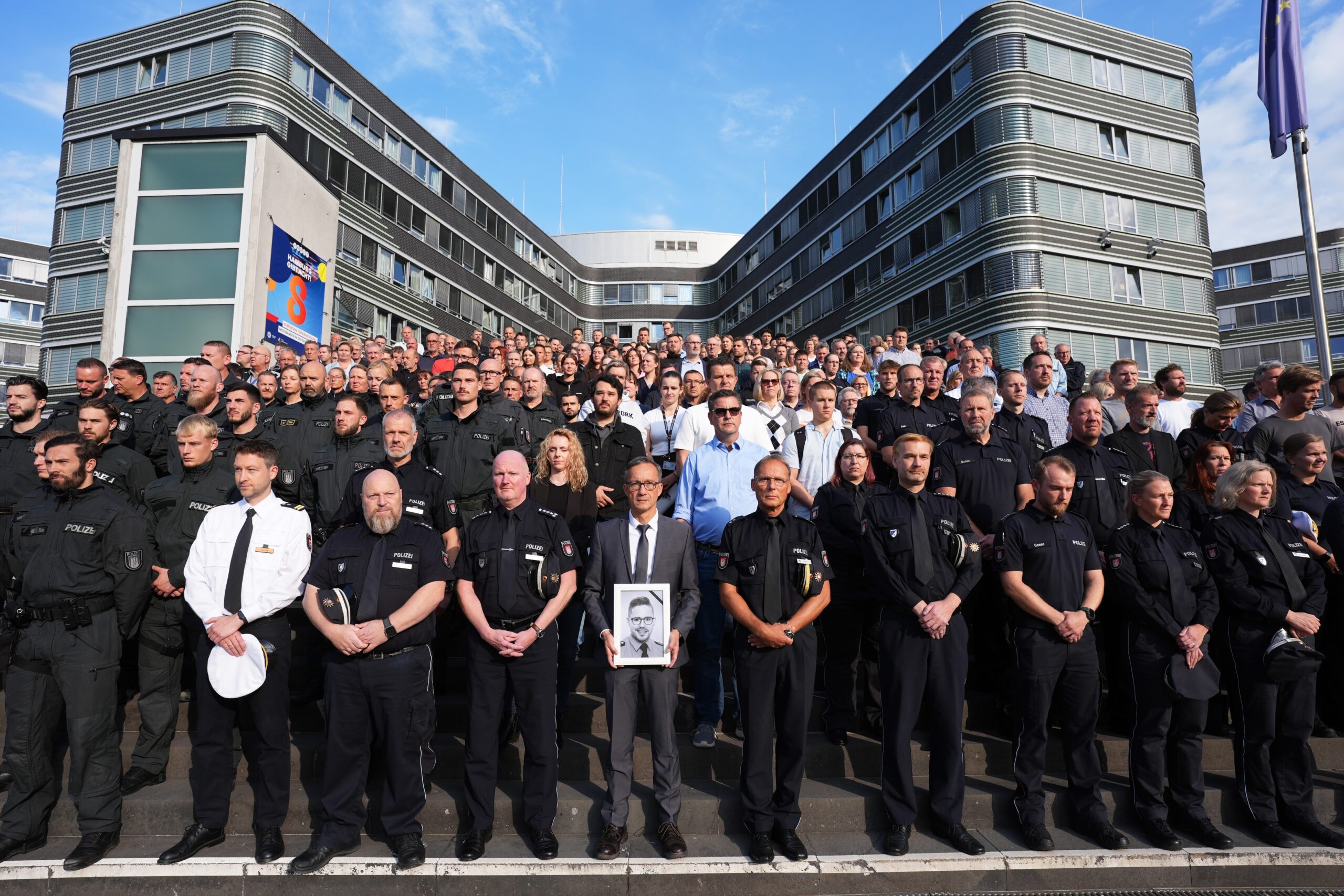 Hamburgs Polizeipräsident Falk Schnabel (vorne, M.), hält ein Foto des im Saarland getöteten Polizeioberkommissars Simon B. während einer Schweigeminute auf der Treppe vor dem Polizeipräsidium in Winterhude.