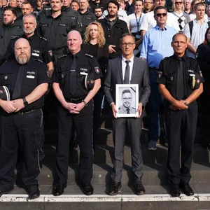 Hamburgs Polizeipräsident Falk Schnabel (vorne, M.), hält ein Foto des im Saarland getöteten Polizeioberkommissars Simon B. während einer Schweigeminute auf der Treppe vor dem Polizeipräsidium in Winterhude.
