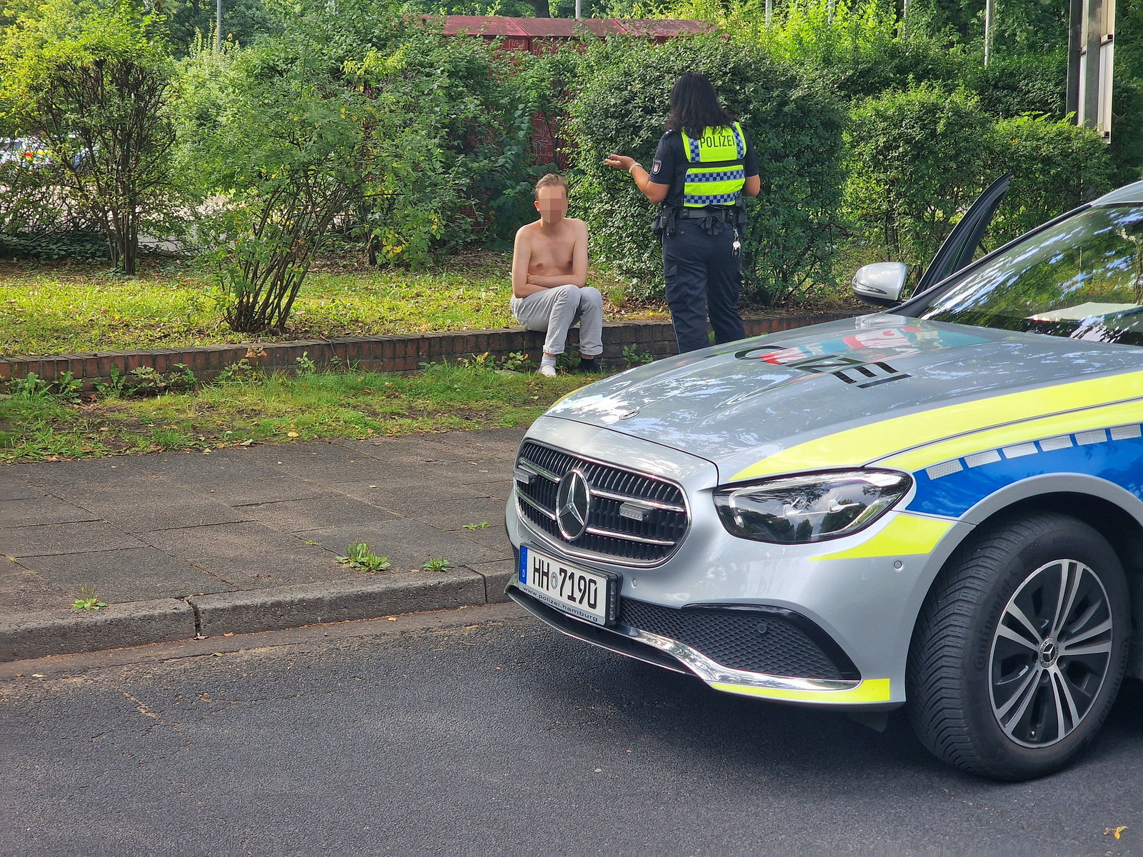 Einer der beiden Streithähne sitzt halbnackt vor dem Haus.
