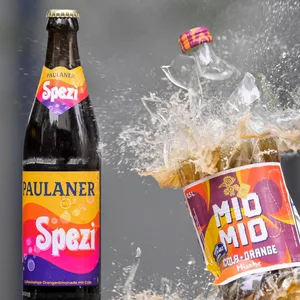 Eine Spezi-Flasche des Herstellers Paulaner (l) steht neben einer zerberstenden Flasche Mio-Mio-Cola-Orange-Mische des Herstellers Berentzen (r).