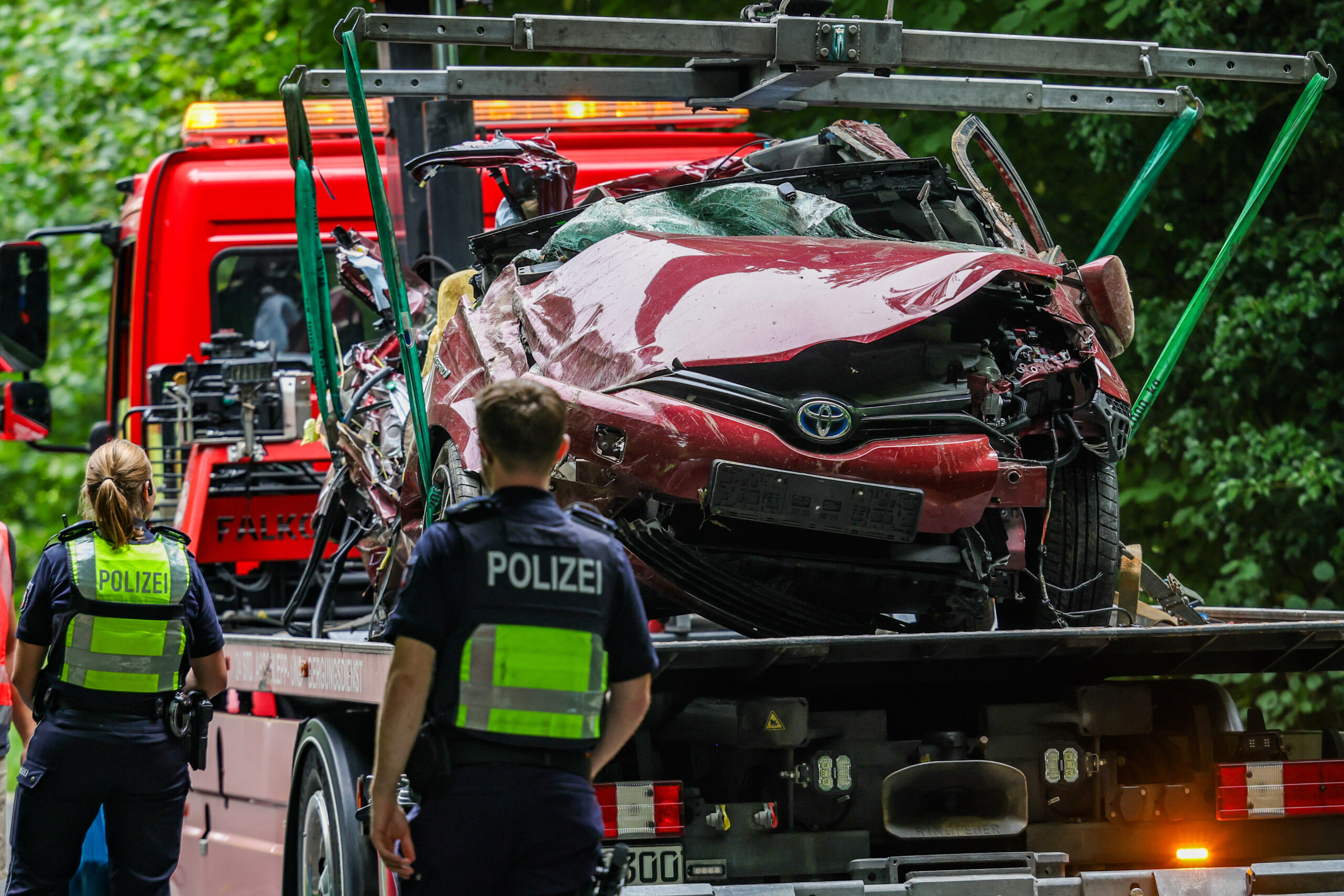 Das Autowrack steht nach der Bergung auf einem Abschleppfahrzeug, Polizeibeamte schauen sich das Fahrzeug an.