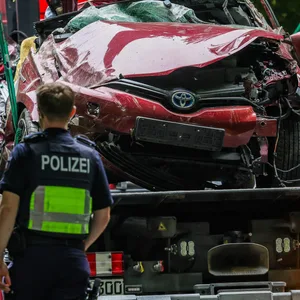 Das Autowrack steht nach der Bergung auf einem Abschleppfahrzeug, Polizeibeamte schauen sich das Fahrzeug an.