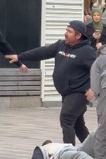 Ein Zeuge mit schwarzem Pulli und schwarzer Cap steht hinter einem Mann, der am Boden liegt.