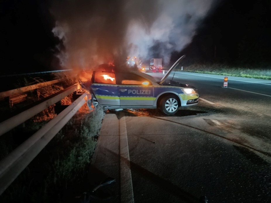 Der Streifenwagen am Rande der Fahrbahn steht in Flammen.