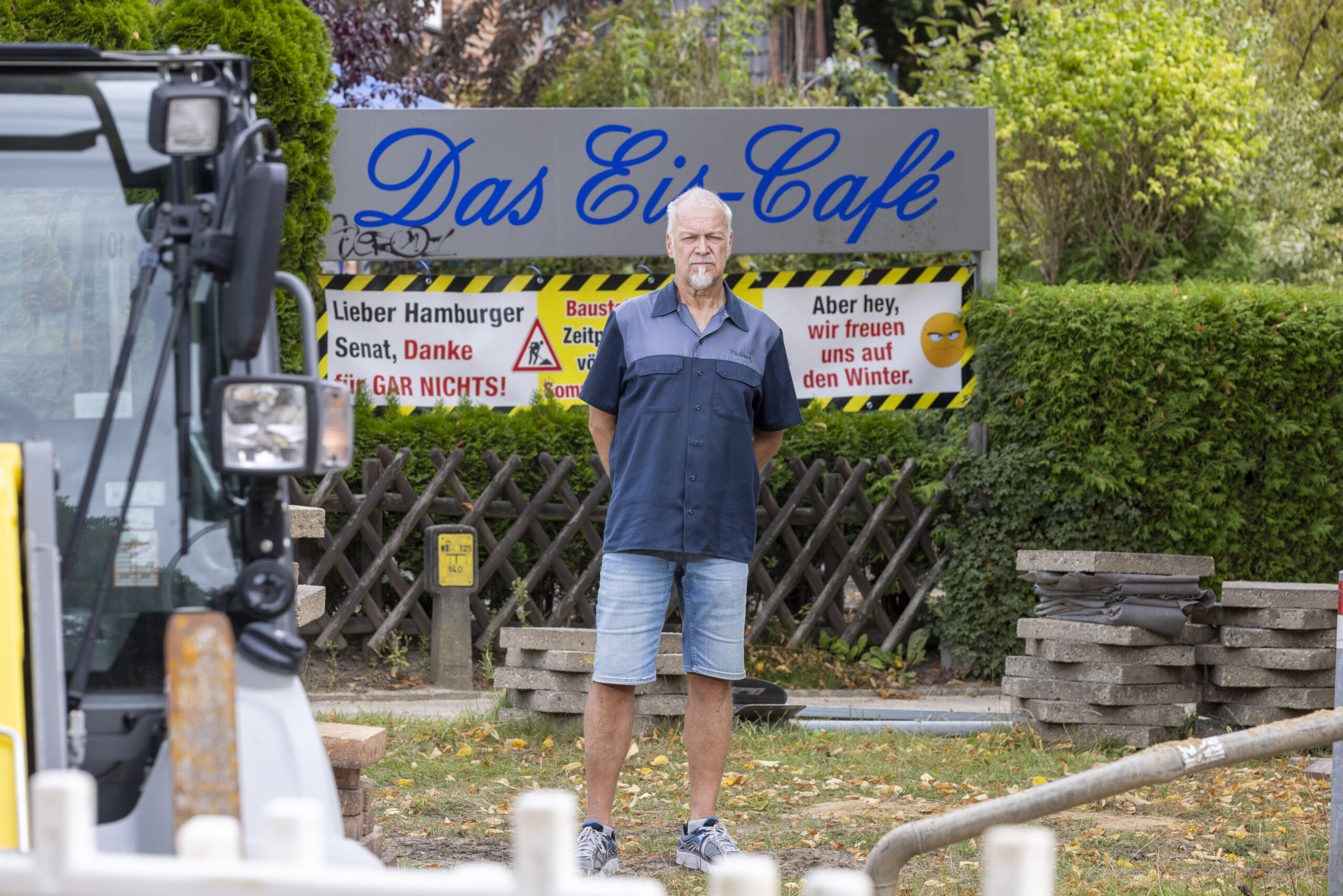 Jens Schöning steht vor seinem Ladenschild auf einer Baustelle. Links im Bild ist ein Bagger zu erkennen.