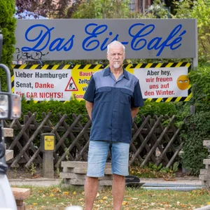 Jens Schöning steht vor seinem Ladenschild auf einer Baustelle. Links im Bild ist ein Bagger zu erkennen.