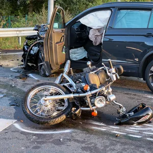 Das beschädigte Motorrad liegt auf der Seite. Daneben steht der Pkw, mit dem es kollidierte.