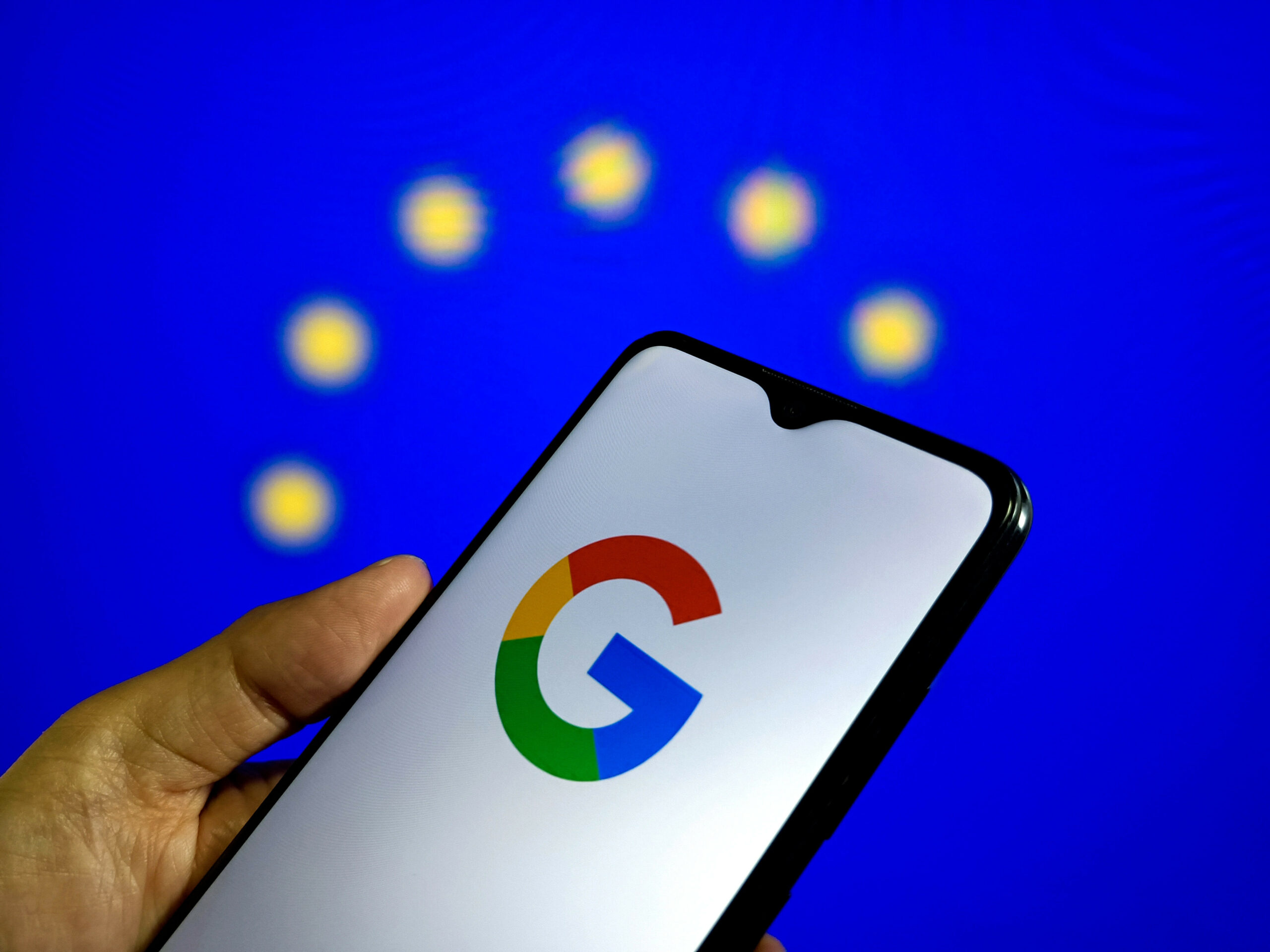 Das Google-Logo ist auf einem Smartphone zu sehen. Im Hintergrund ist die EU-Flagge.