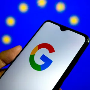 Das Google-Logo ist auf einem Smartphone zu sehen. Im Hintergrund ist die EU-Flagge.