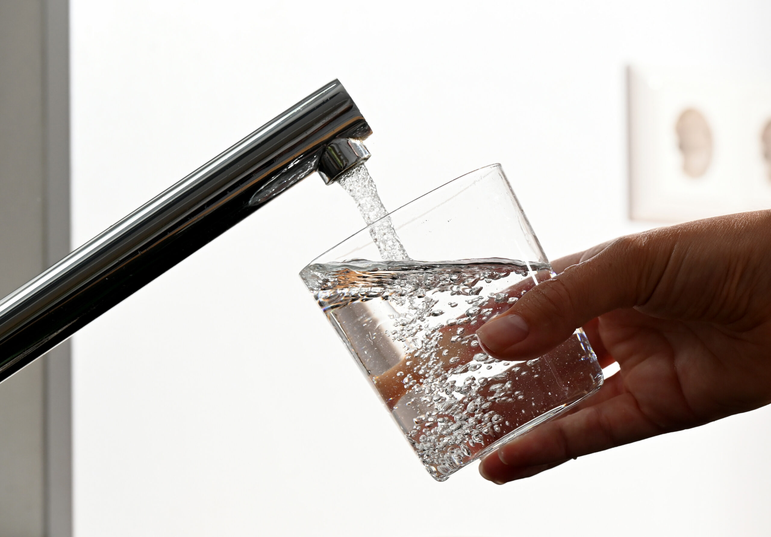 Eine Hand hält ein Wasserglas unter einen Wasserhahn.