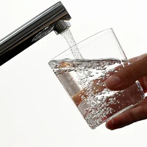 Eine Hand hält ein Wasserglas unter einen Wasserhahn.