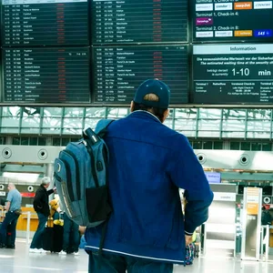 Ein Mann mit Rucksack steht vor der Anzeigetafel des Hamburger Flughafens.