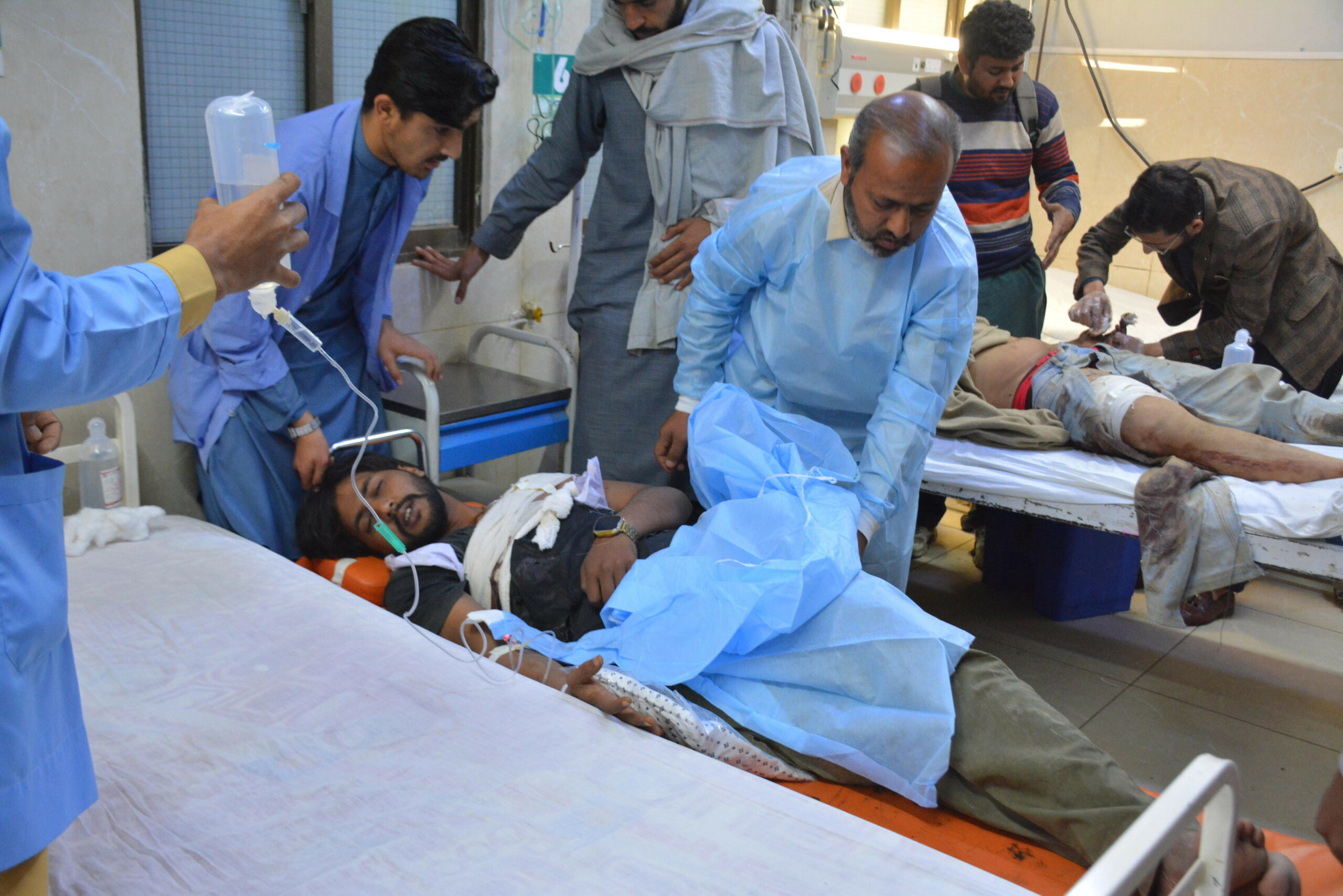 Zwei Männer liegen auf Krankenhausliegen und werden von medizinischem Personal versorgt.