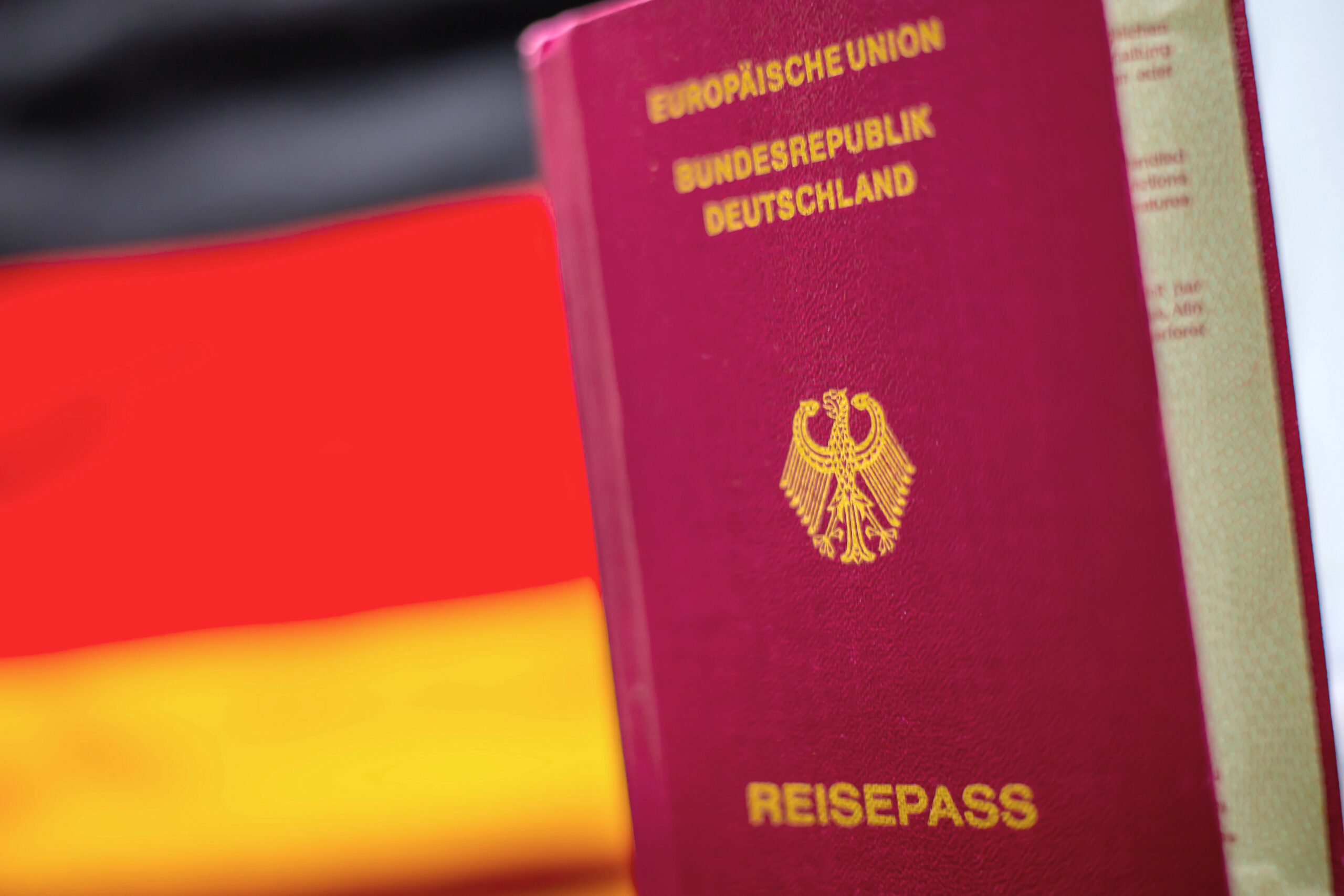Ein Reisepass ist vor den Farben schwarz rot gold der deutschen Fahne zu sehen.