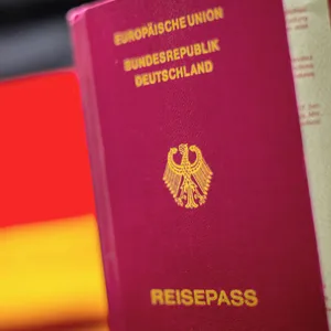 Ein Reisepass ist vor den Farben schwarz rot gold der deutschen Fahne zu sehen.