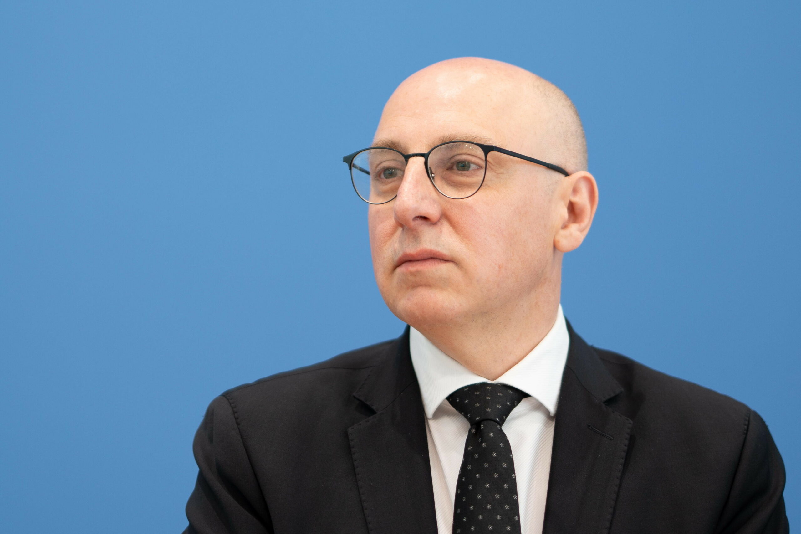 Sinan Selen sitzt vor einer blauen Wand