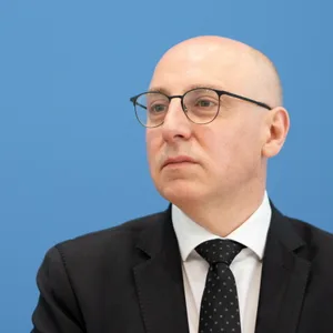 Sinan Selen sitzt vor einer blauen Wand