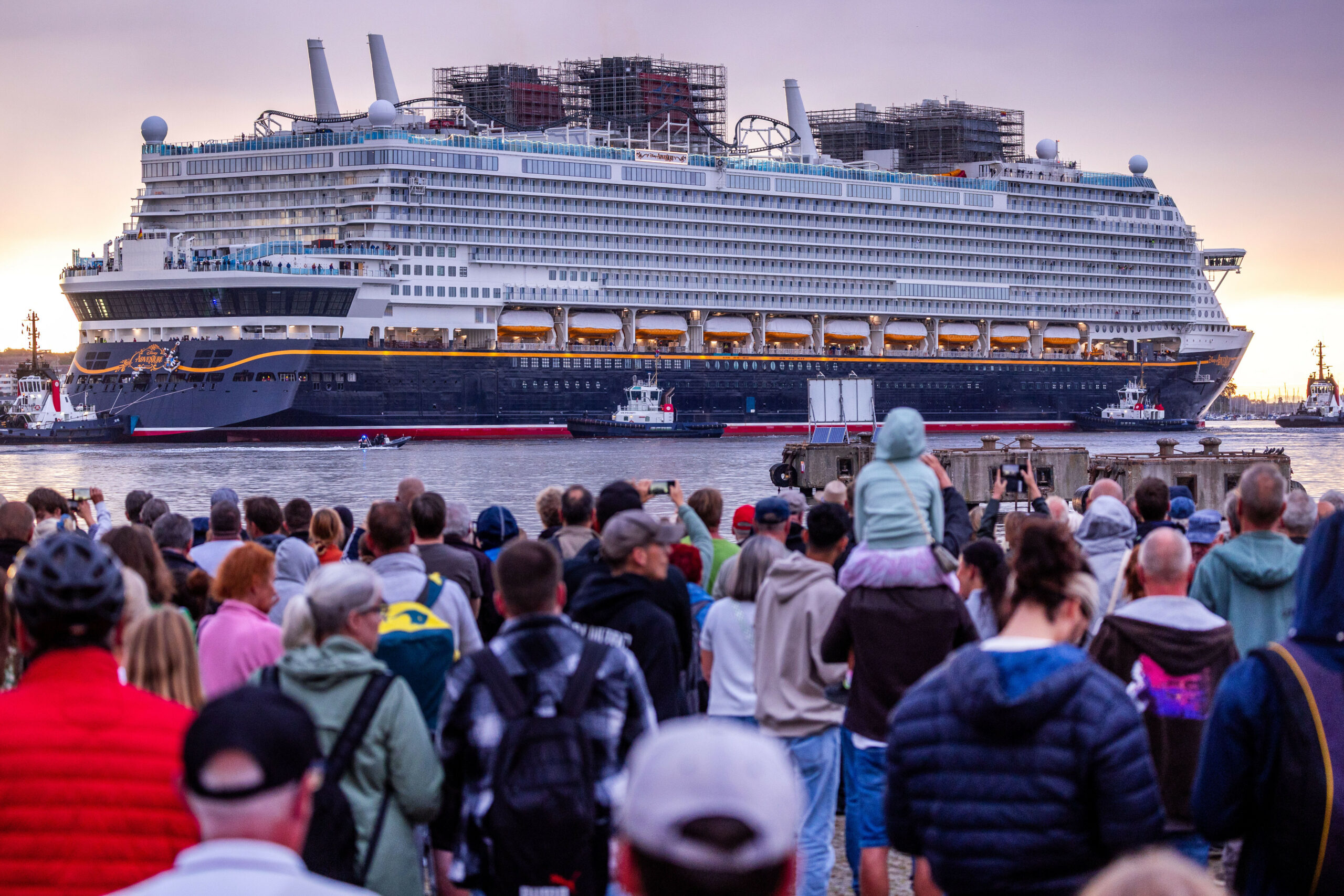 Hunderte Menschen beobachten das in der Wismarer Werft gebaute Kreuzfahrtschiff „Disney Adventure“ beim Auslaufen in Richtung Ostsee.